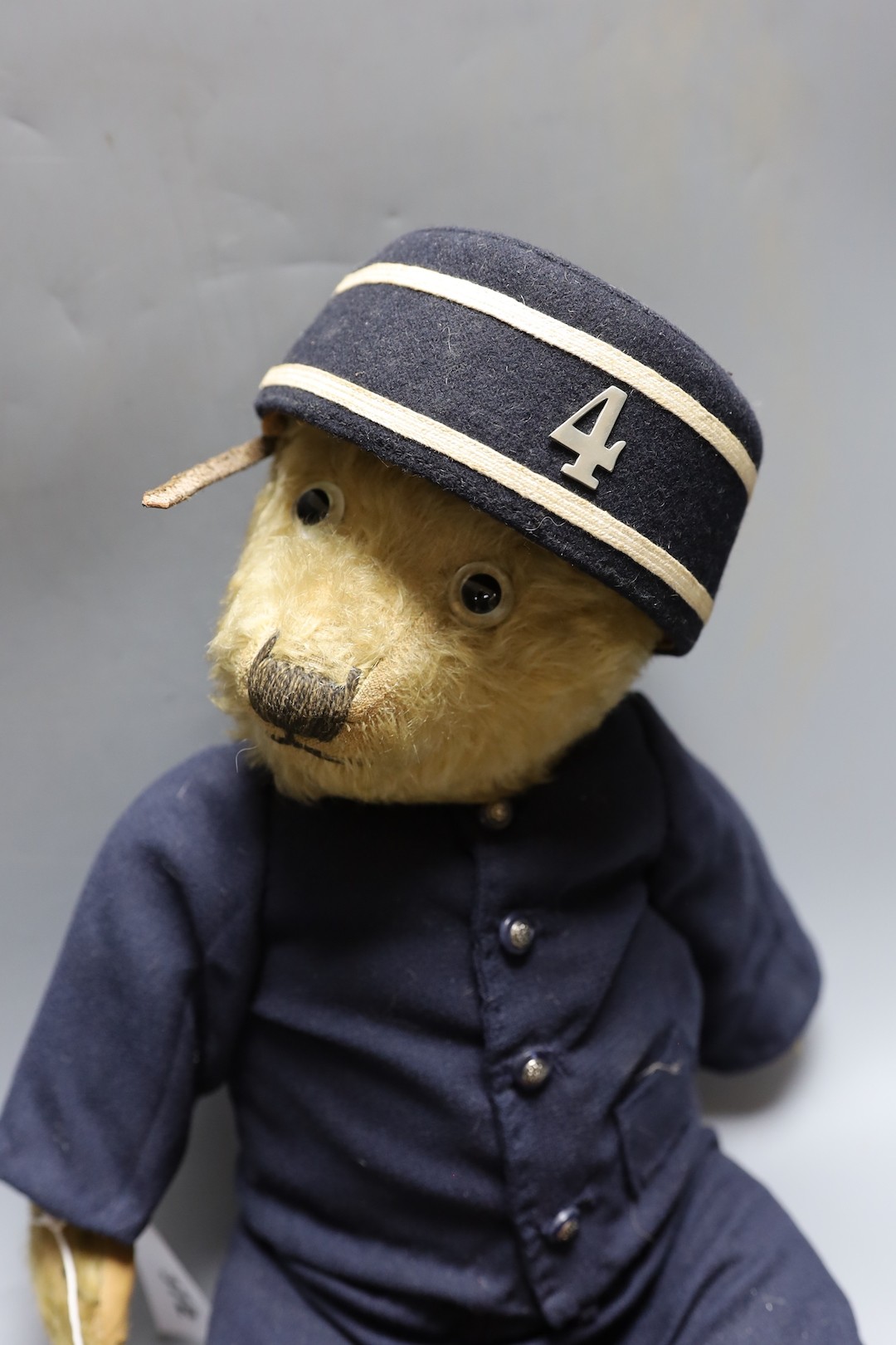 A Chiltern teddy bear dressed as railway porter, replaced footpads, thinning of mohair to tummy and arms together with miniature leather trunk